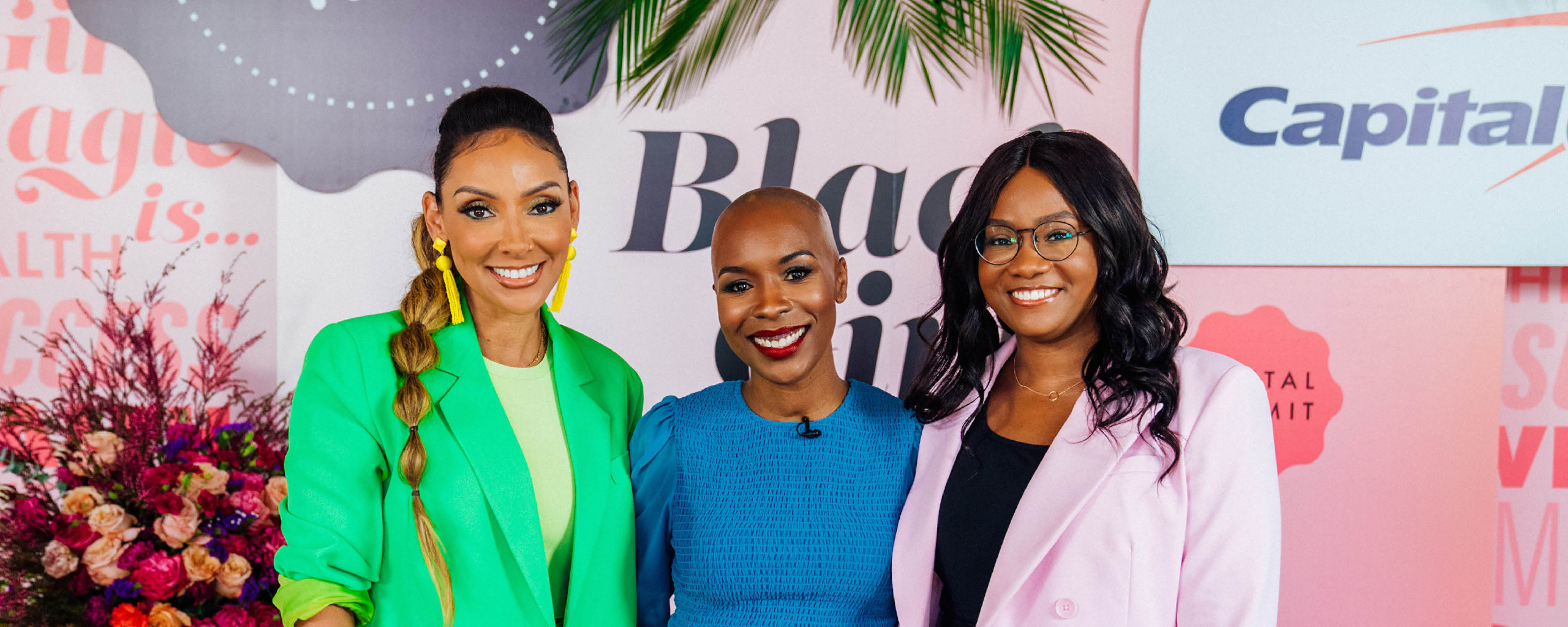 Three Capital One associates stand at the Black Girl Magic event in colorful outfits, standing in front of the Capital One Black Girl Magic Sign